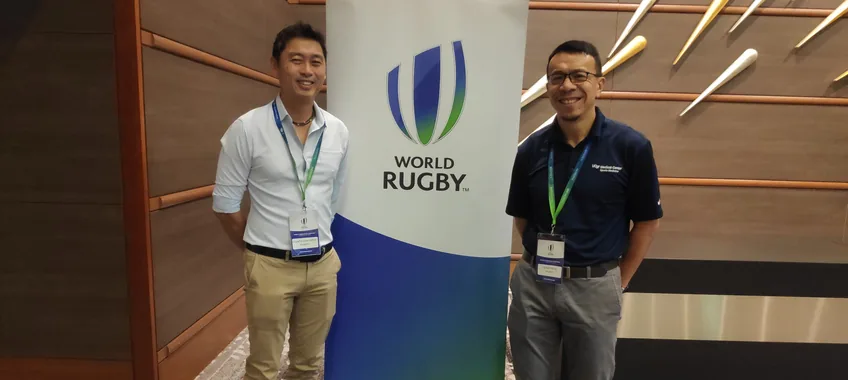 Dr Lai dan seorang rekan di samping spanduk World Rugby pada sebuah acara tahun 2019